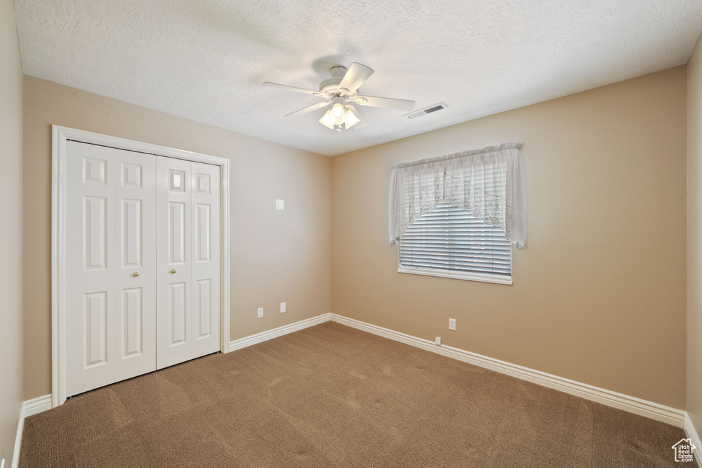 Unfurnished bedroom with carpet, a closet, ceiling fan, and a textured ceiling