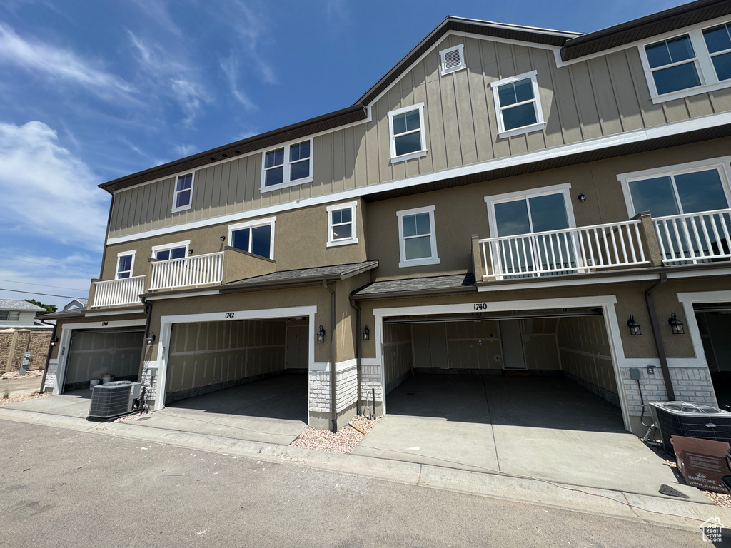 View of front facade with a garage, a balcony, board and batten siding, and stucco siding