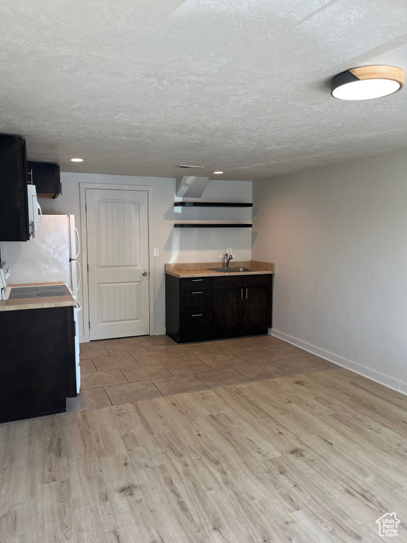 Kitchen featuring light wood finished floors, light countertops, white appliances, a textured ceiling, and dark cabinets