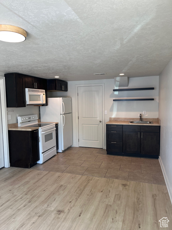 Kitchen with white appliances, light wood-style flooring, open shelves, dark cabinets, and light countertops