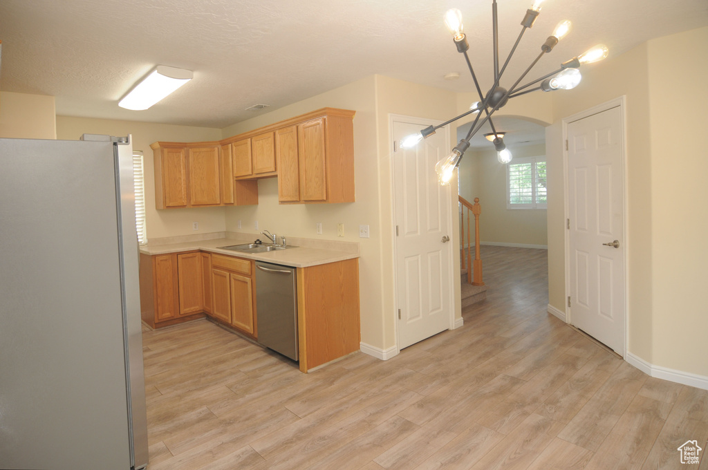 Kitchen with freestanding refrigerator, dishwasher, a chandelier, light countertops, and light wood-style flooring