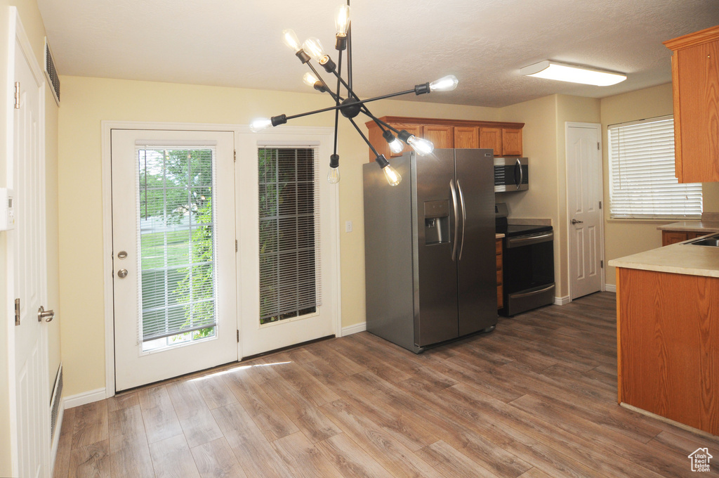 Kitchen with stainless steel appliances, brown cabinets, a chandelier, wood finished floors, and light countertops