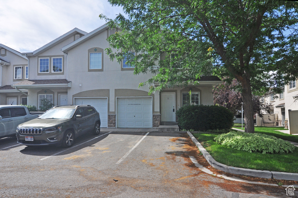 View of property with stucco siding, a garage, driveway, and stone siding