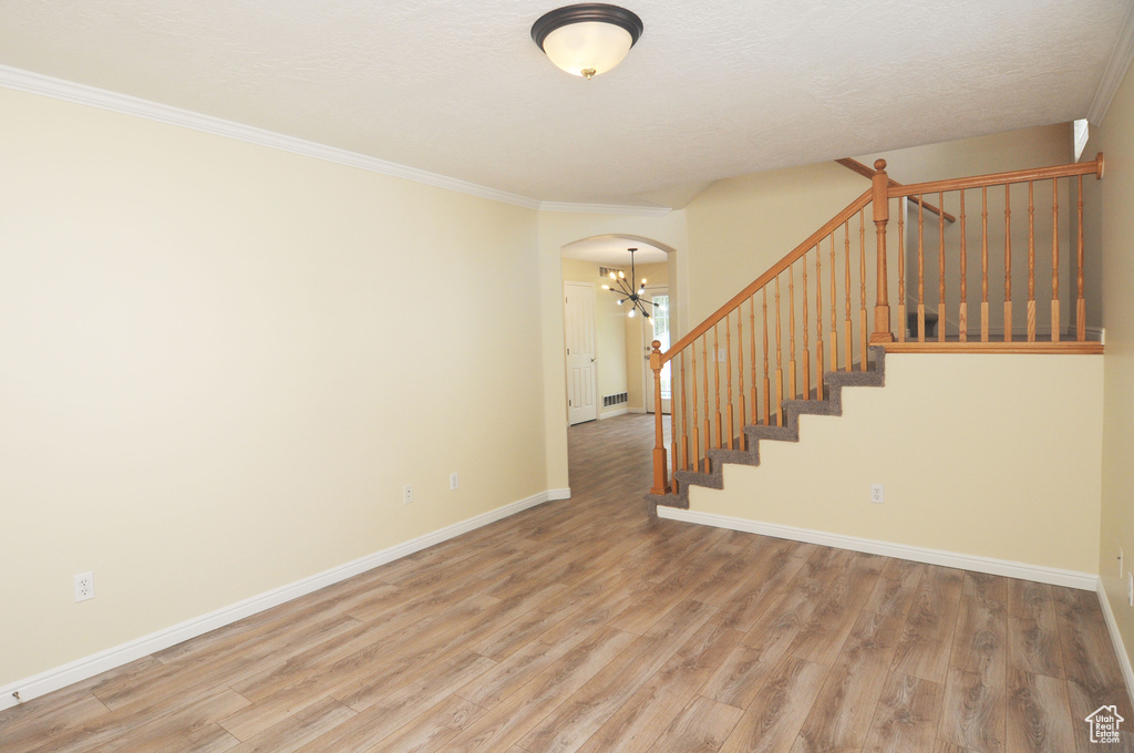 Stairs with a chandelier, arched walkways, wood finished floors, and crown molding