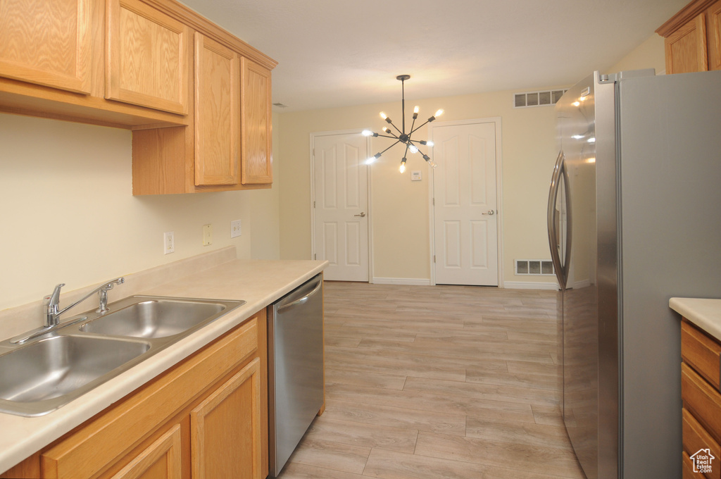Kitchen with stainless steel appliances, a chandelier, light wood-style floors, light countertops, and hanging light fixtures