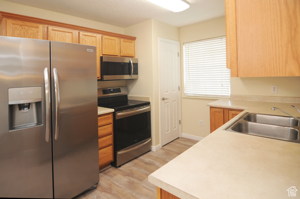 Kitchen with appliances with stainless steel finishes, light wood-style flooring, light countertops, and light brown cabinetry