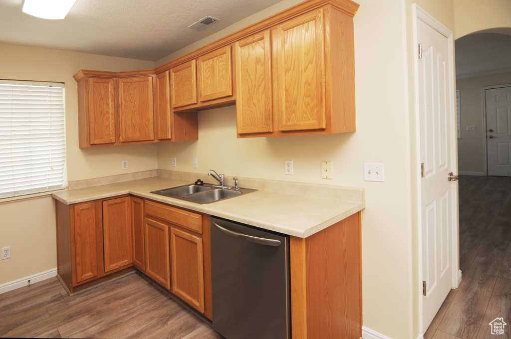 Kitchen with stainless steel dishwasher, wood finished floors, light countertops, and arched walkways