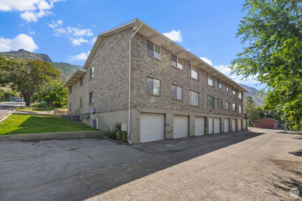 View of side of property featuring a mountain view, community garages, and a yard
