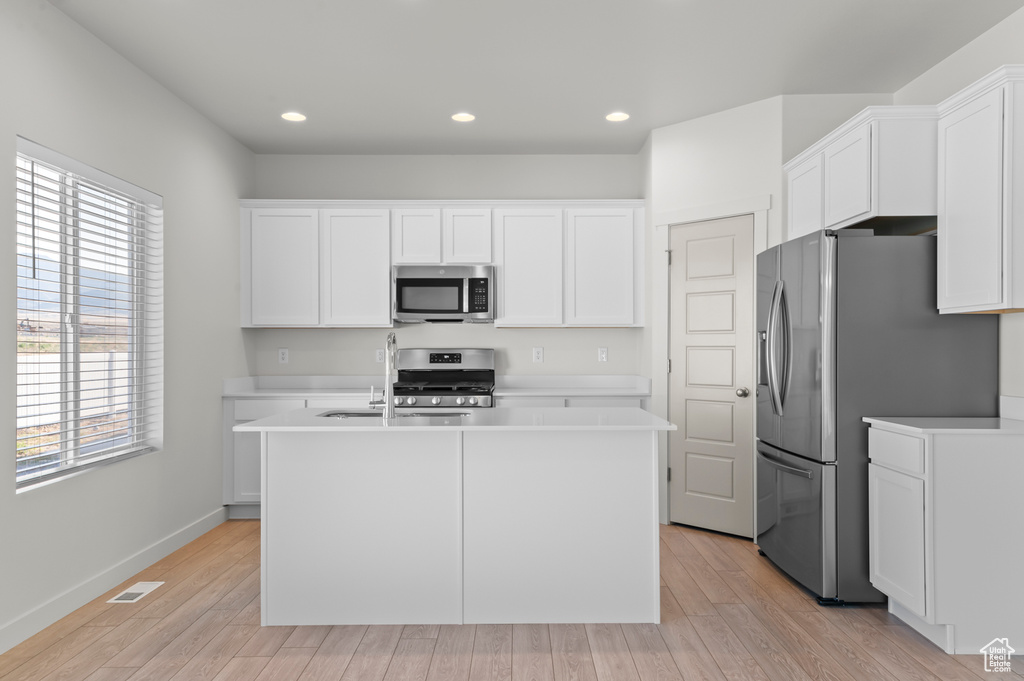 Kitchen with appliances with stainless steel finishes, white cabinets, a center island with sink, and recessed lighting