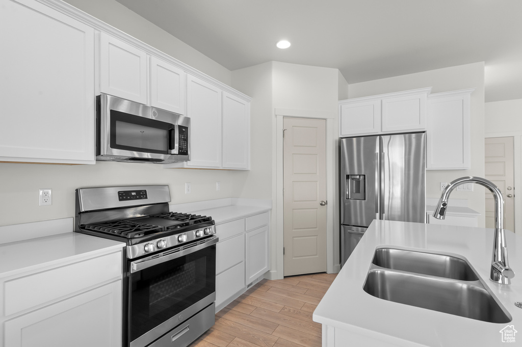 Kitchen featuring stainless steel appliances, light countertops, white cabinets, light wood-type flooring, and recessed lighting