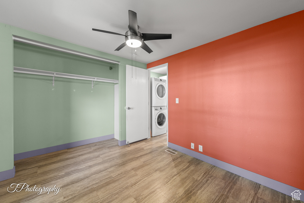 Laundry area with stacked washer / drying machine, wood finished floors, and a ceiling fan