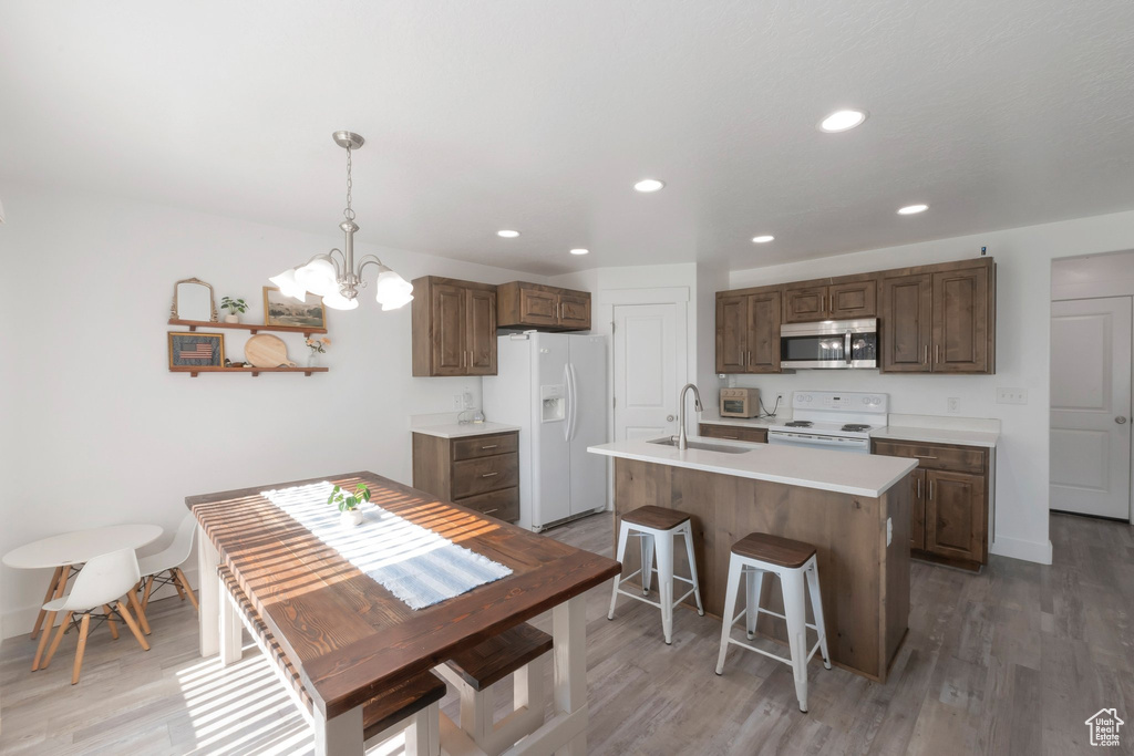 Kitchen with white appliances, a chandelier, light countertops, light wood-style flooring, and recessed lighting