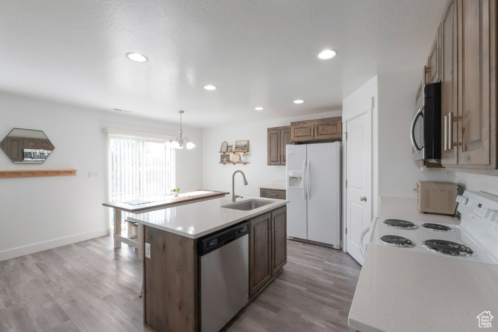 Kitchen featuring white appliances, light countertops, light wood-style floors, a chandelier, and an island with sink