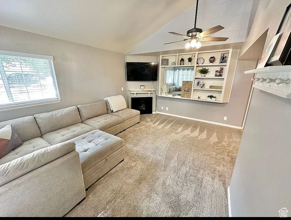 Living area featuring a ceiling fan, vaulted ceiling, a fireplace, and carpet floors