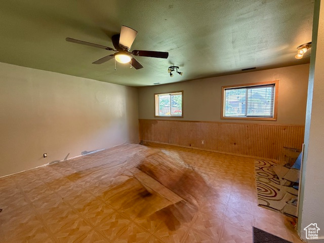 Unfurnished room featuring wainscoting, ceiling fan, and wood walls