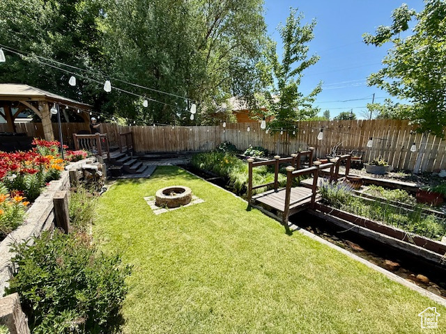 Fenced backyard featuring a fire pit, a vegetable garden, and a gazebo