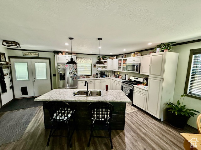 Kitchen with appliances with stainless steel finishes, dark wood-style flooring, white cabinets, decorative light fixtures, and a kitchen bar