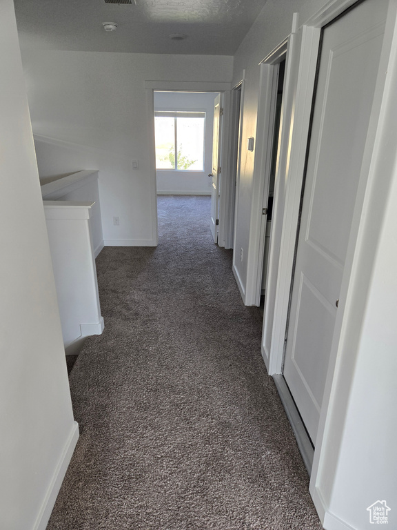 Hallway with dark colored carpet and an upstairs landing