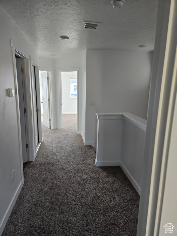 Hallway featuring carpet, an upstairs landing, and a textured ceiling