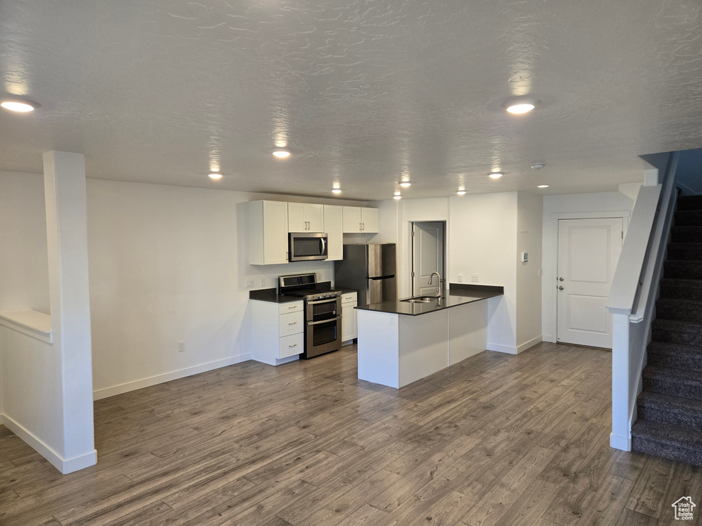 Kitchen featuring stainless steel appliances, dark countertops, dark wood finished floors, a peninsula, and recessed lighting