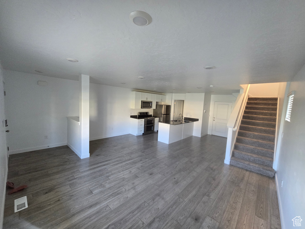 Unfurnished living room featuring dark wood-style floors and stairs
