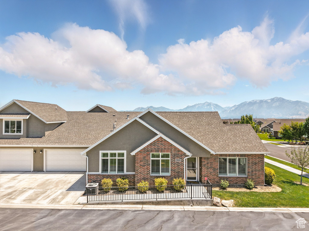 View of front of house with brick siding, roof with shingles, a mountain view, concrete driveway, and stucco siding