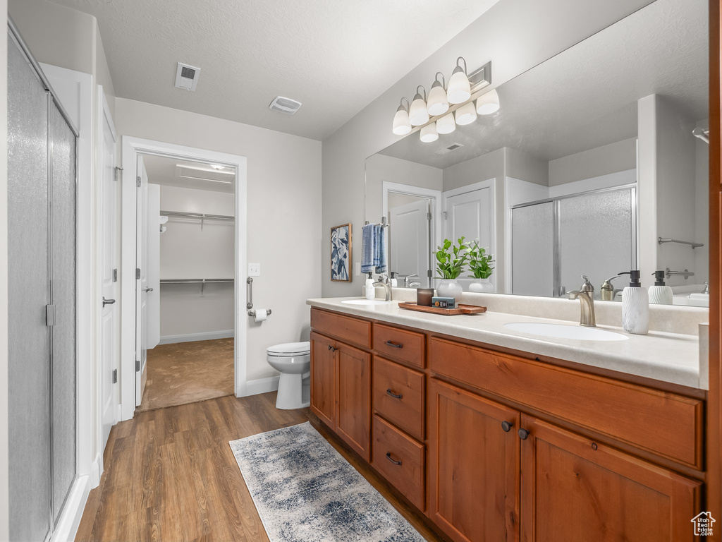 Bathroom featuring a shower stall, double vanity, wood finished floors, and a walk in closet