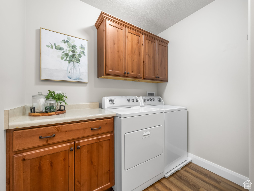 Laundry area with cabinet space, separate washer and dryer, wood finished floors, and a textured ceiling
