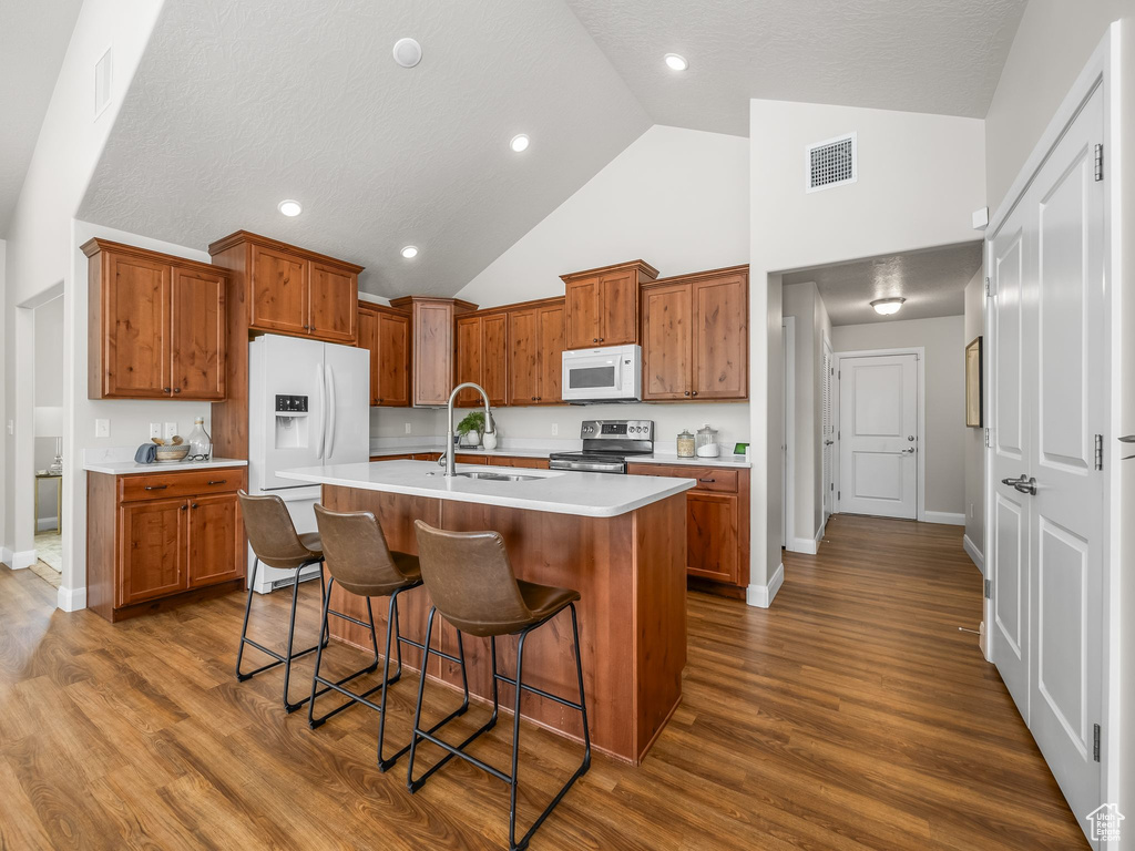 Kitchen with white appliances, brown cabinets, light countertops, a kitchen island with sink, and a kitchen breakfast bar