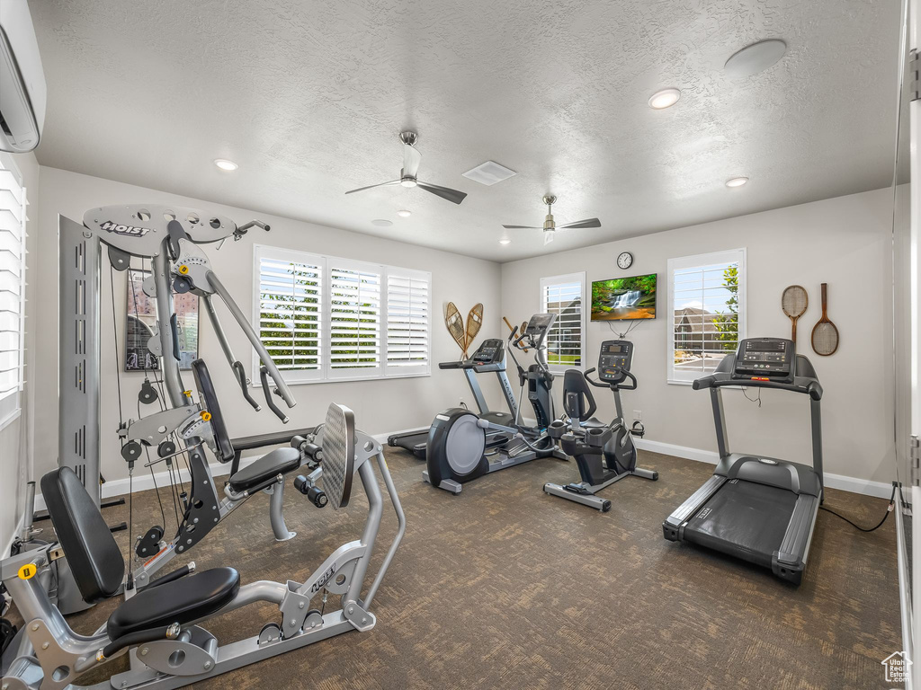 Exercise room with an AC wall unit, plenty of natural light, a textured ceiling, carpet floors, and a ceiling fan