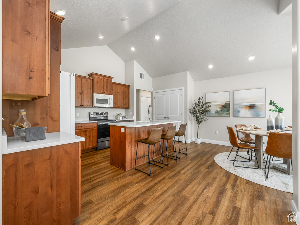 Kitchen with electric range, white microwave, a breakfast bar, high vaulted ceiling, and a center island with sink