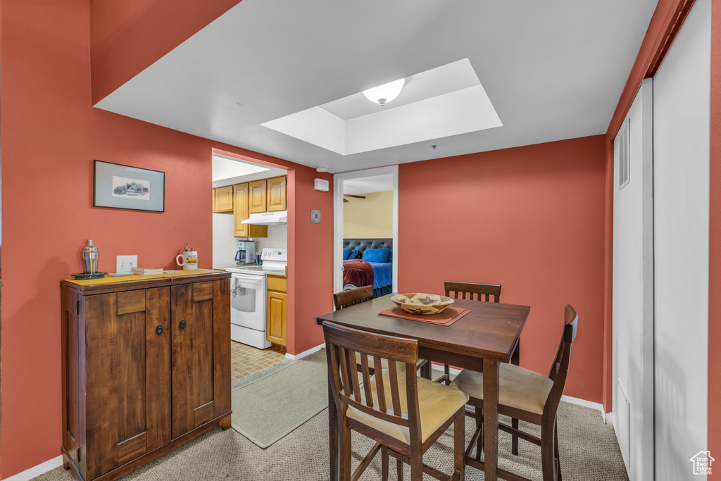 Dining space featuring a raised ceiling, a skylight, and light colored carpet