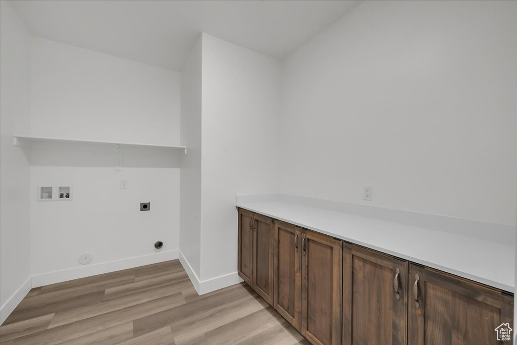 Laundry area featuring hookup for an electric dryer, washer hookup, light wood-style floors, and cabinet space