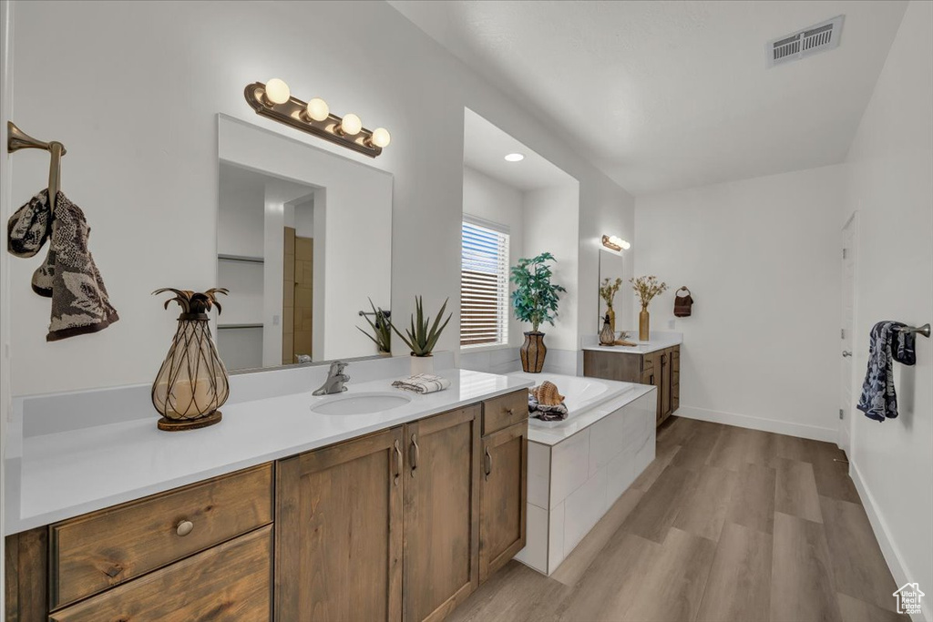 Bathroom featuring two vanities, wood finished floors, and a bath