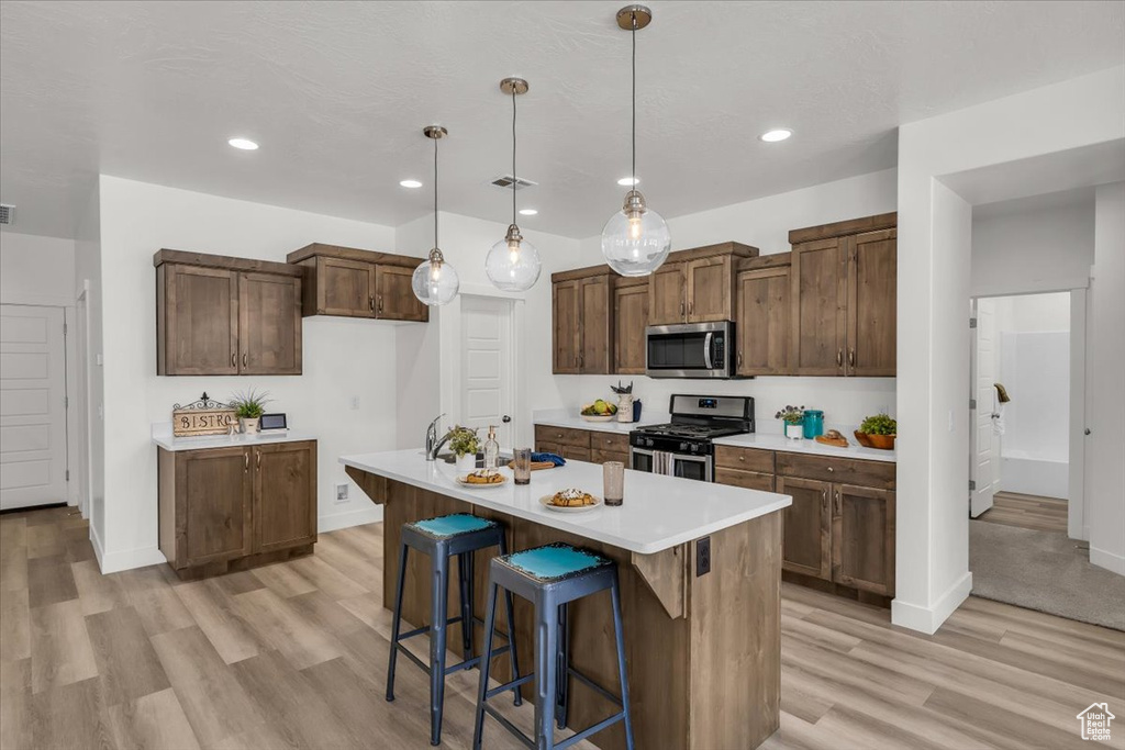 Kitchen with stainless steel appliances, light wood-type flooring, light countertops, hanging light fixtures, and recessed lighting