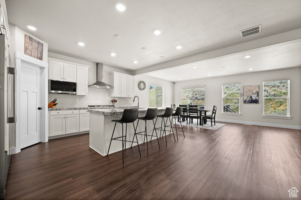 Kitchen featuring wall chimney range hood, appliances with stainless steel finishes, dark wood finished floors, a breakfast bar, and recessed lighting