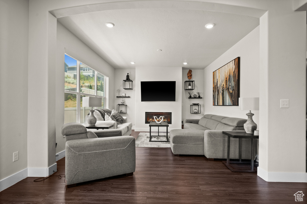 Living room featuring dark wood-style flooring, a glass covered fireplace, and recessed lighting