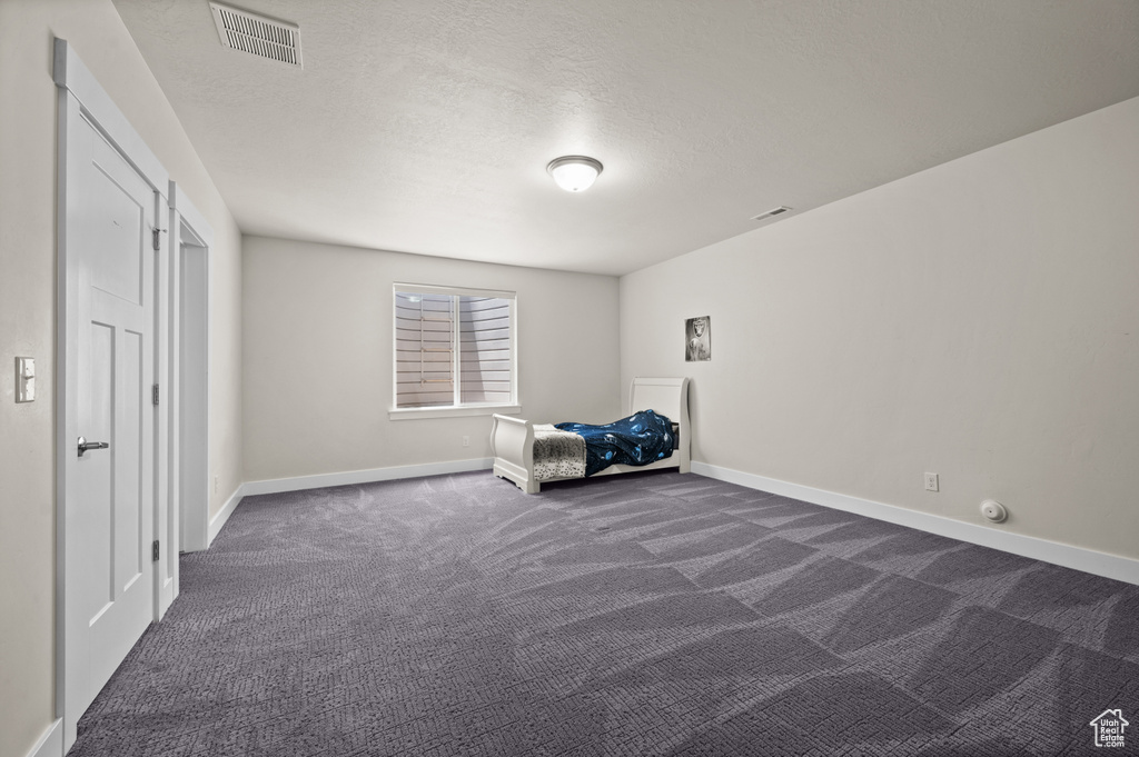Unfurnished bedroom with dark carpet and a textured ceiling