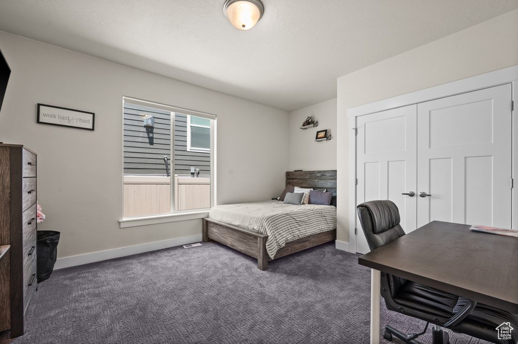 Bedroom featuring dark colored carpet, a desk, and a closet