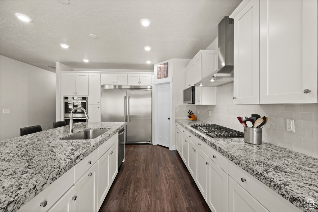 Kitchen featuring stainless steel appliances, wall chimney exhaust hood, dark wood finished floors, white cabinets, and tasteful backsplash