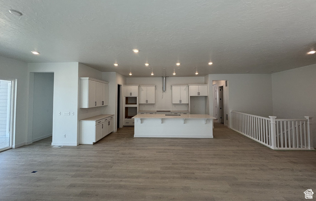 Kitchen with a spacious island, wood finished floors, white cabinets, open floor plan, and a textured ceiling