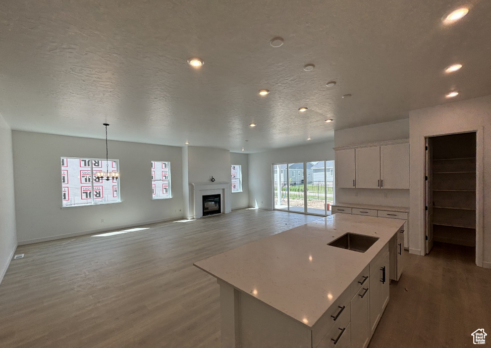 Kitchen featuring wood finished floors, white cabinetry, a glass covered fireplace, a chandelier, and a center island with sink