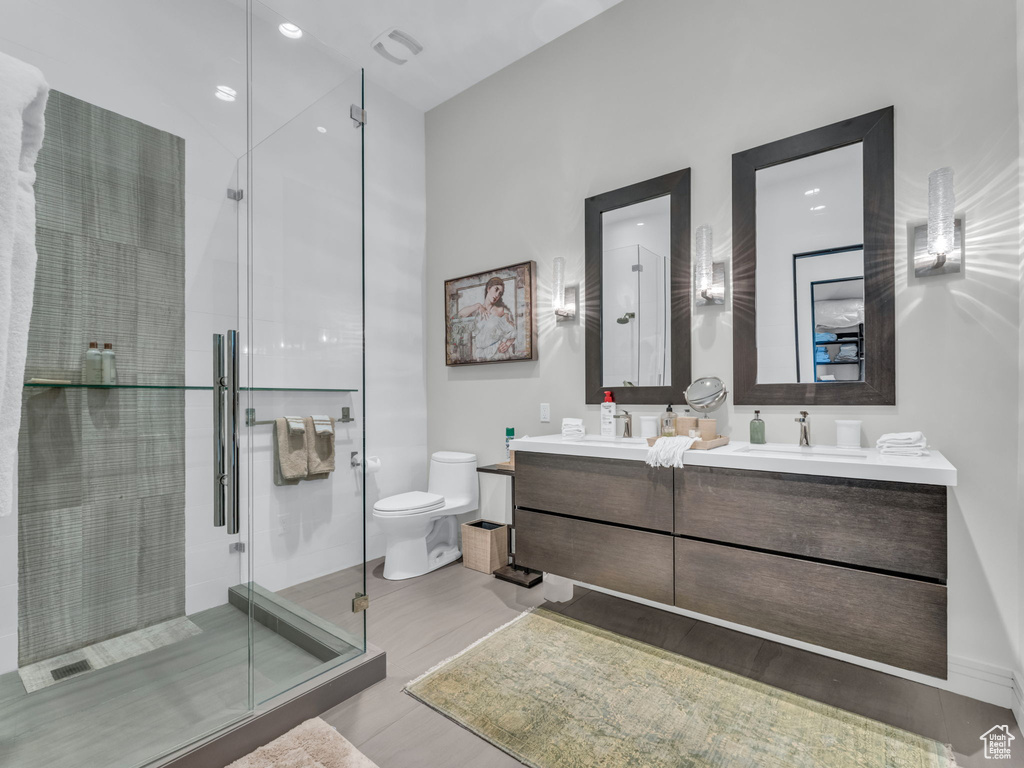 Bathroom with double vanity, wood finished floors, and a stall shower