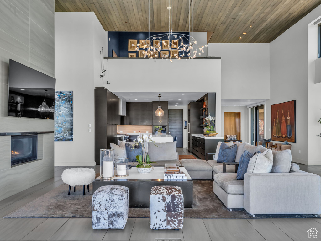 Living room featuring a high ceiling, wood ceiling, a chandelier, a tiled fireplace, and recessed lighting