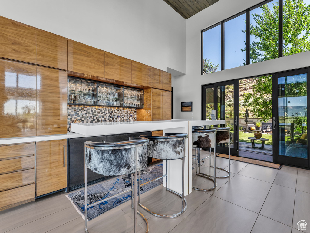 Indoor dry bar with high vaulted ceiling, light tile patterned flooring, and decorative backsplash