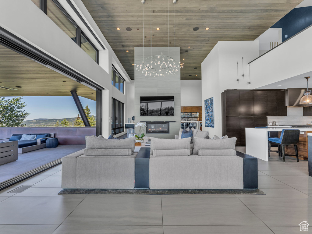 Living room featuring a towering ceiling, a chandelier, light tile patterned flooring, wood ceiling, and a large fireplace