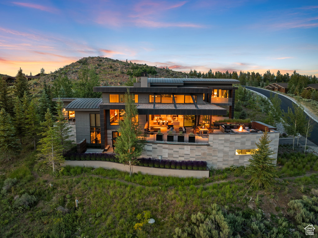 Back of house at dusk with a patio, a metal roof, a standing seam roof, an outdoor living space with a fire pit, and a mountain view