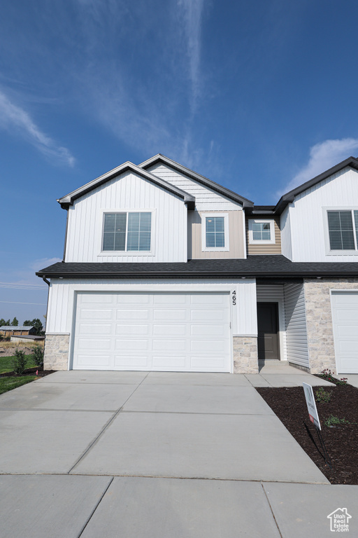 View of front of house featuring stone siding, an attached garage, driveway, and board and batten siding