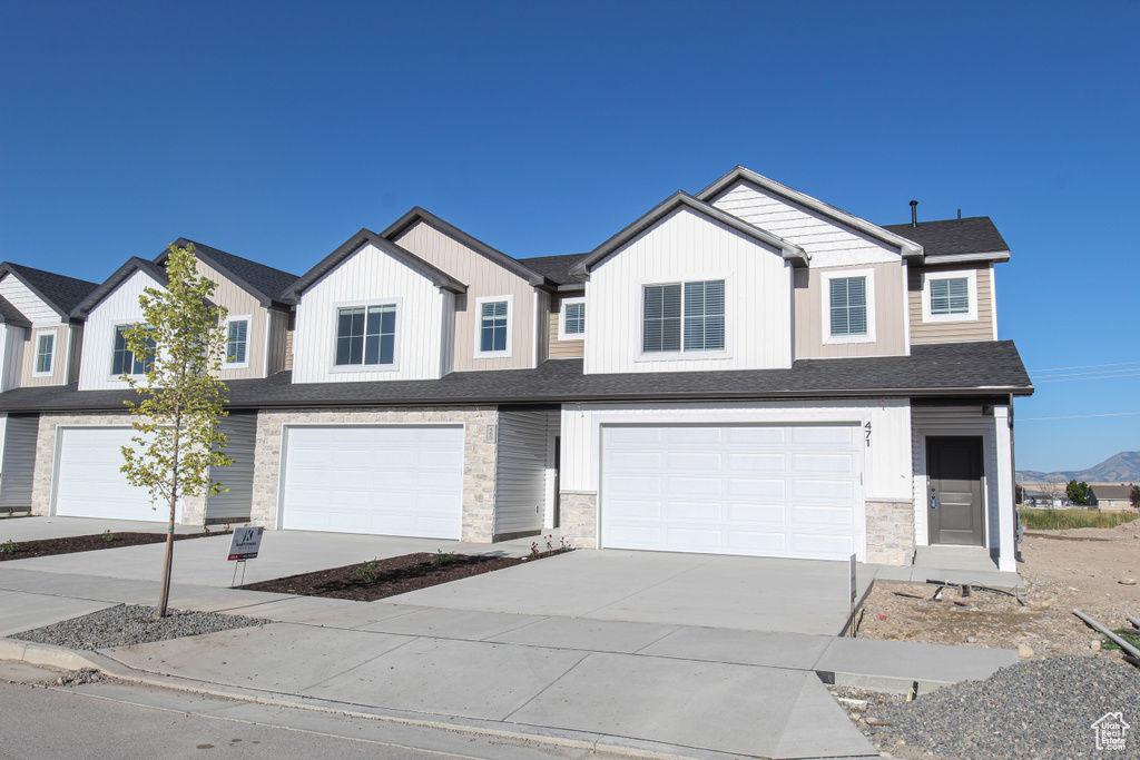 Multi unit property with an attached garage, concrete driveway, and stone siding