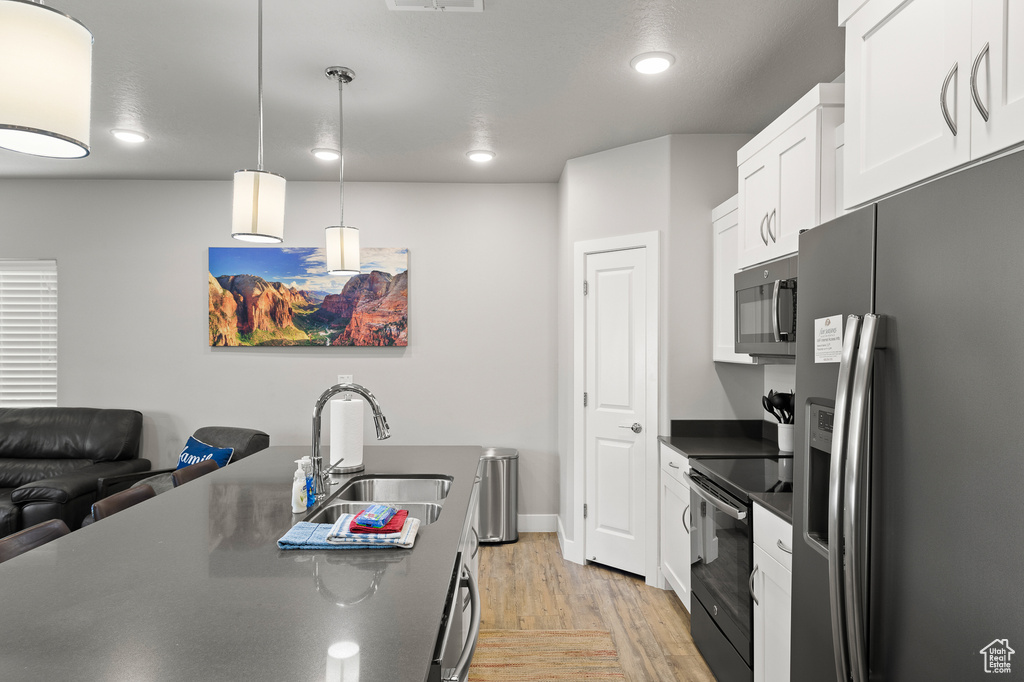 Kitchen with stainless steel appliances, dark countertops, light wood-style floors, white cabinets, and recessed lighting